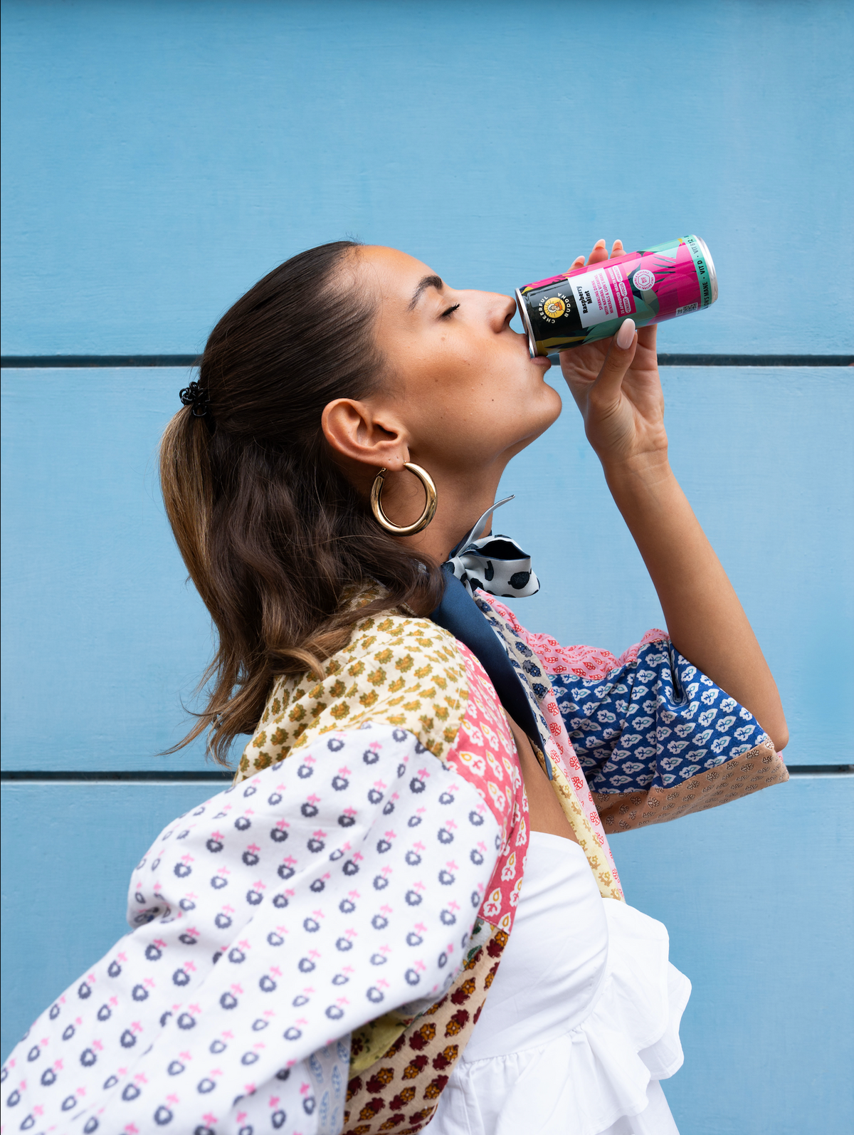 Woman drinking a can of Raspberry & Mint sparkling drink against a blue wall