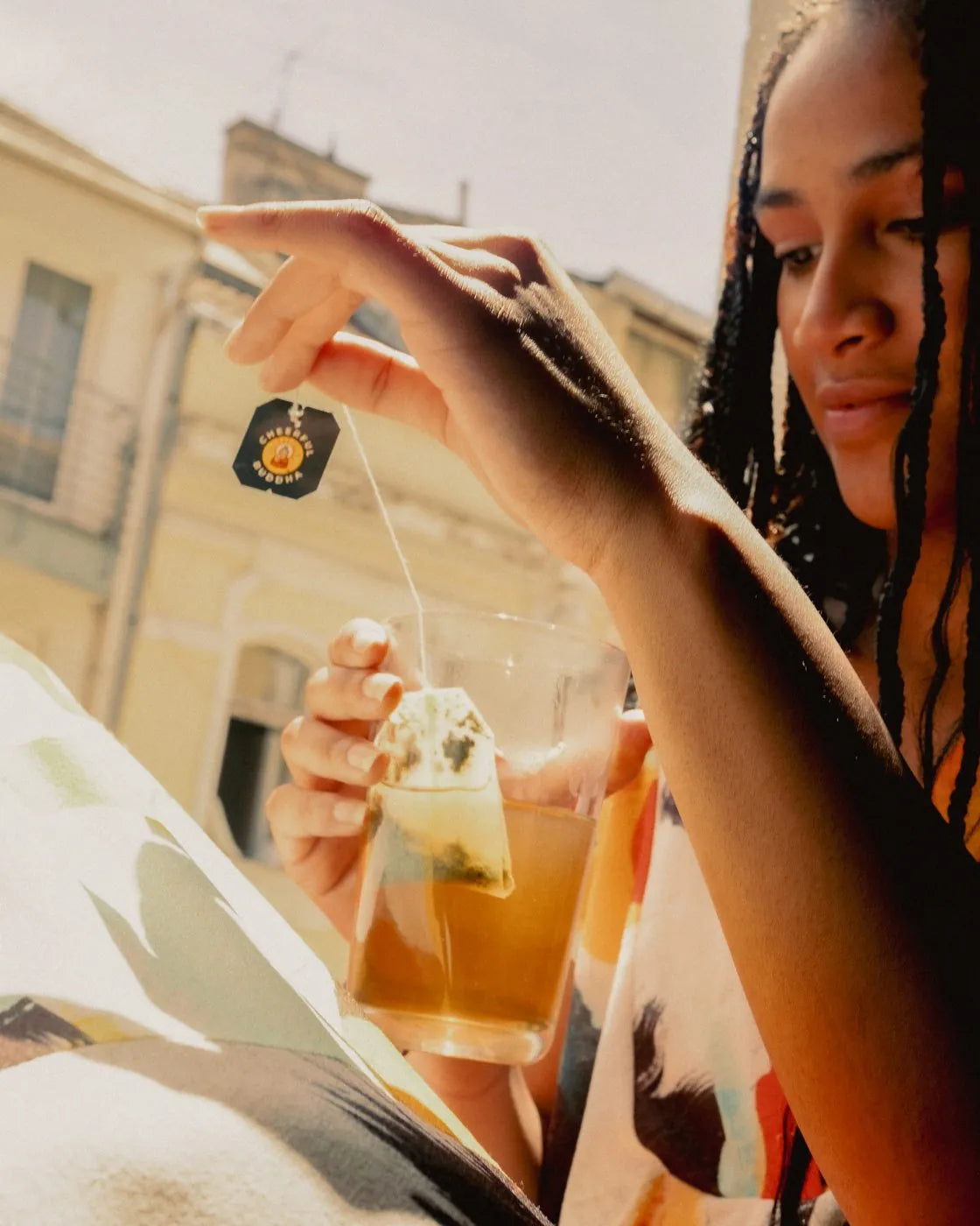 Woman dipping a Lion's Mane tea bag into a glass by a sunny window