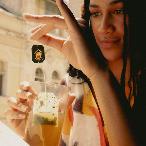 Woman dipping a Cheerful Buddha Lion's Mane tea bag into a glass of hot tea
