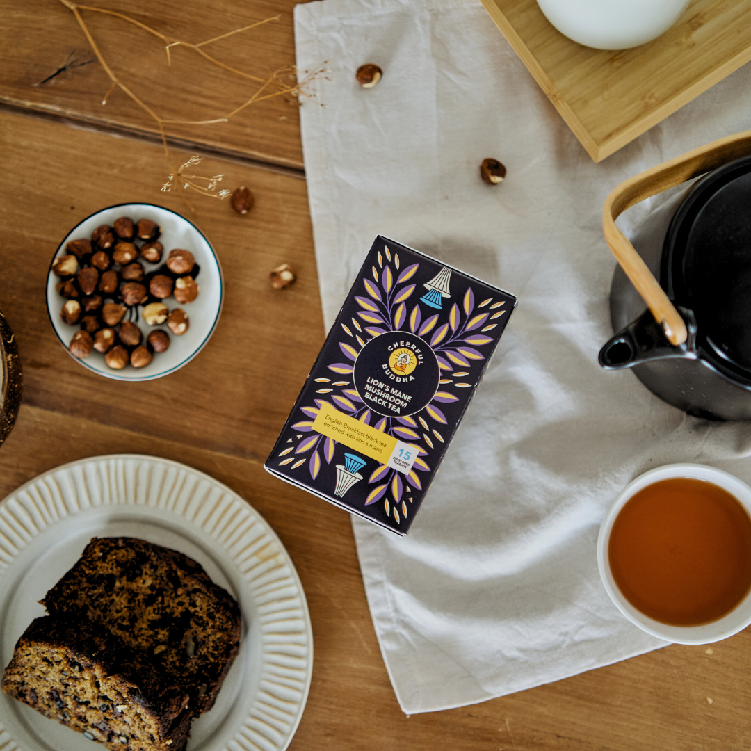 Lion's Mane Black Tea box with a cup of black tea, a teapot and a slice of cake on a wooden table