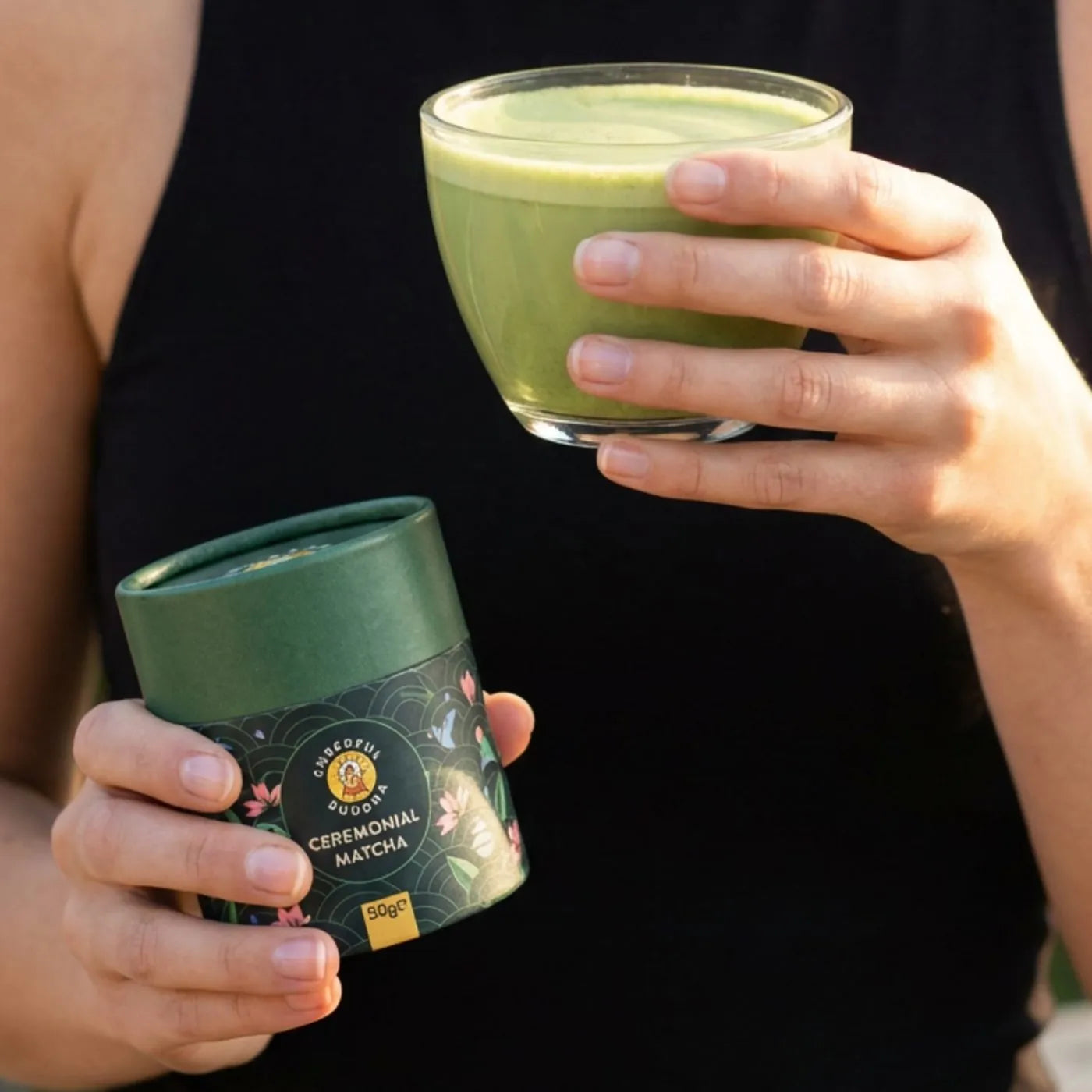 Hand holding a glass of matcha next to the Ceremonial Grade Matcha tube